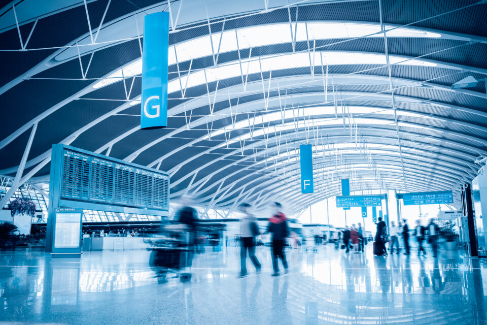 Blue tinted image of a busy airport terminal with travelers walking through