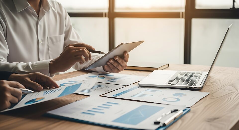 A professional reviewing dashboards on paper and laptop